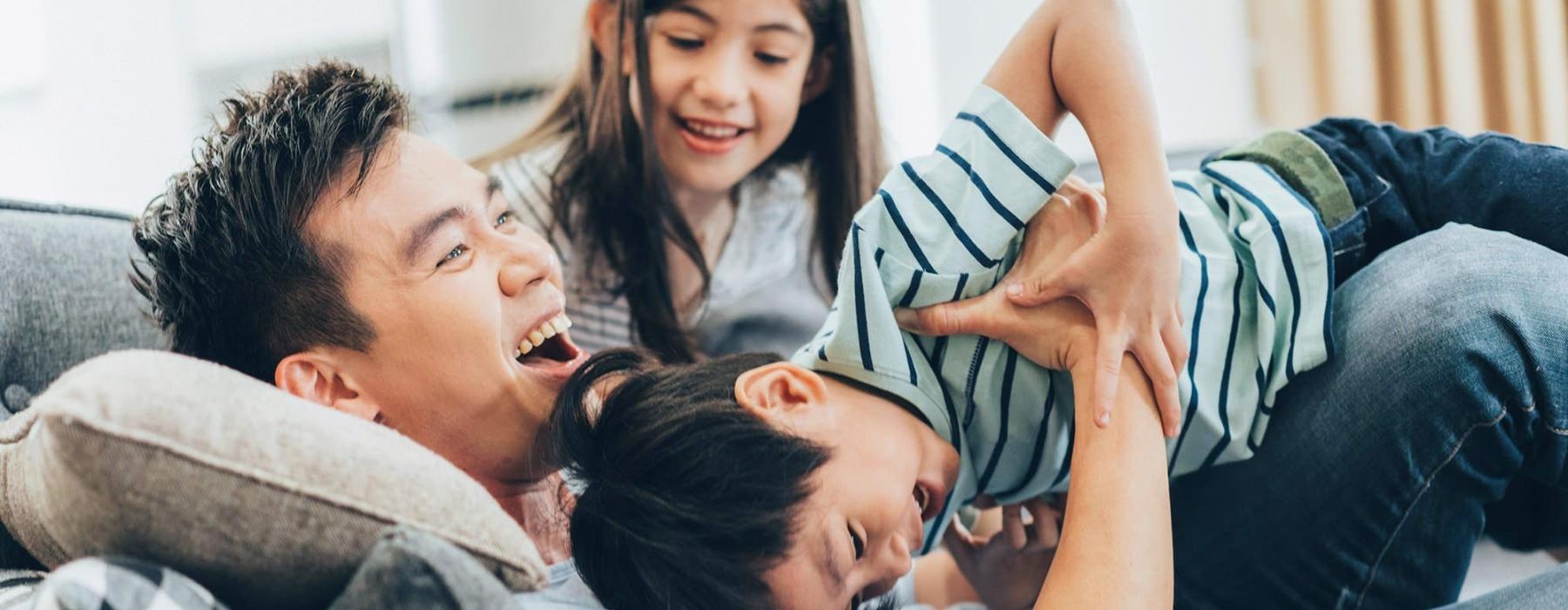 father plays on a couch with his young children